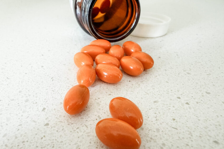 Orange softgel supplements spilled from a brown bottle onto a white countertop